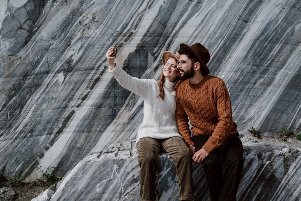 a couple sitting on granite rocks taking a selfie