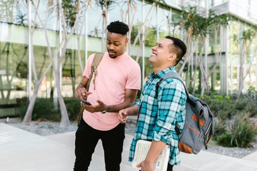 a man using a phone while standing beside a person holding a book